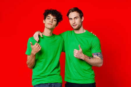 two men hugging in green T-shirts on a red backgroundの写真素材