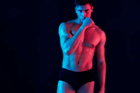 sexy male athlete gesturing with his hands on a black background and neon skin color modelの写真素材
