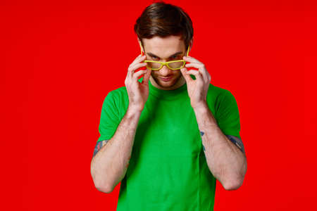 a man in a green t-shirt with tattoos in his hands wearing glasses on a red background