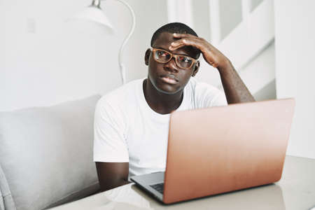 man of african appearance at home at the table in front of laptop workingの写真素材