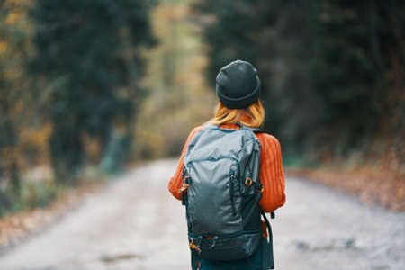 woman with a backpack in a hat and an orange sweater on the road in the autumn forest back viewの写真素材