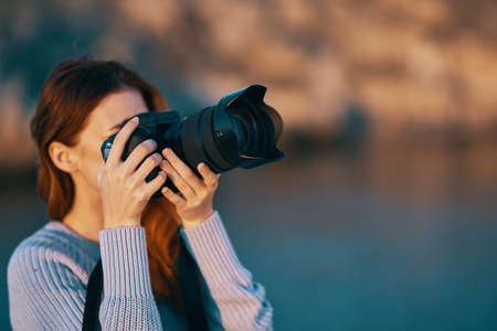 woman holding a camera with a lens in nature in the mountains and the seaの写真素材
