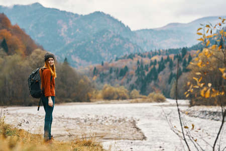 woman on the river bank in the mountains in the autumn forest in nature back view