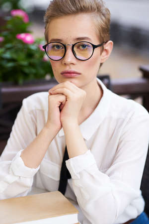 young woman in a shirt and glasses with a book at a table in a cafeの写真素材