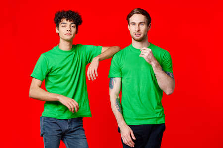 Two cheerful friends in green t-shirts joy of communication red backgroundの写真素材