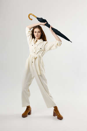 Woman in white overalls holding an umbrella above her head protection from rain studio