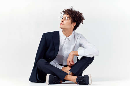 curly-haired guy in fashionable clothes and sneakers sits on the floor in a bright room in full growthの写真素材
