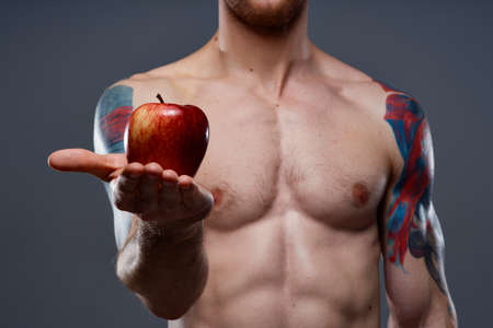 tattooed athlete holding red apple on gray background naked torso cropped viewの写真素材