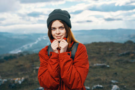 happy woman in a red jacket with a backpack and in a hat mountains in the background fresh airの写真素材