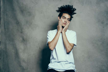 Cheerful guy with curly hair gestures with his hands near his face on a gray fabric background in a...