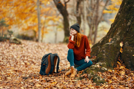 woman near tree and backpack for travel fallen leaves autumn forestの写真素材