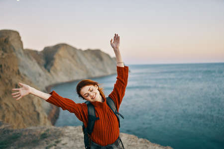 happy traveler in the mountains near the sea gestures with her hands and a backpack on her backの写真素材