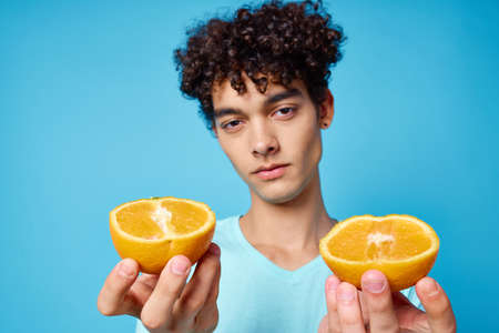 man with curly hair holding oranges fruit blue backgroundの写真素材