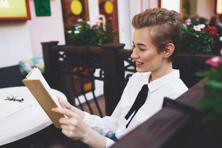woman reading a book at a table in a cafe notepad female student jeans sneakers shirt