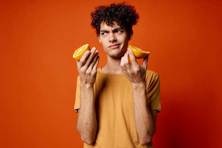 guy with curly hair oranges in hands fruit fun red backgroundの写真素材