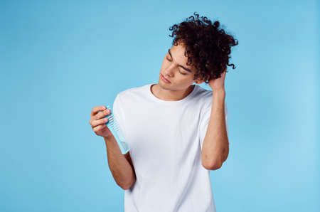 cute man with curly hair holding comb in hand and blue background cropped viewの写真素材