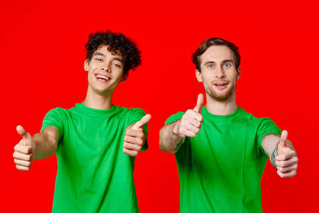 Cheerful friends in green t-shirts gesturing with hands emotions red background