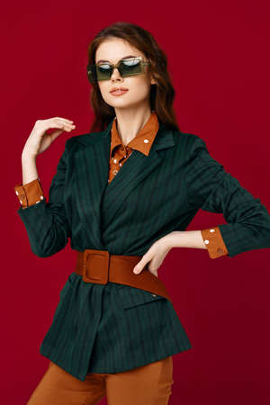 brunette wearing sunglasses jacket fashion clothing posing red background