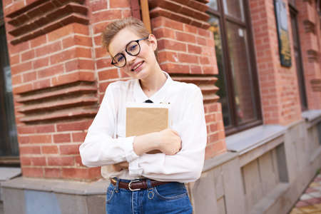 woman near a brick building in glasses with a book in her hands on the street education institute