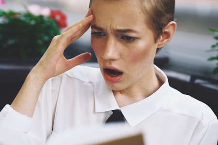 emotional woman with short hair reading a book in a restaurant and pink flowers in the backgroundの写真素材