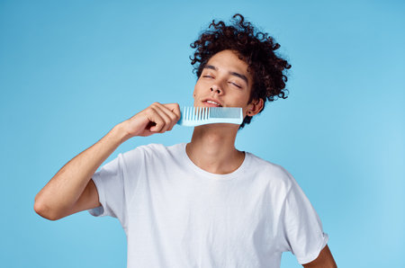 guy model with a comb in his hand and curly hair blue background portraitの写真素材