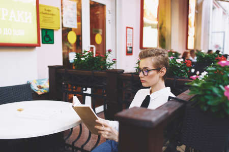 woman at the table with book in hand glasses on the face of cafe interior street summer