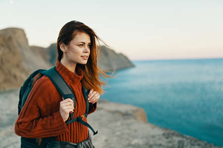 beautiful woman in a sweater with a backpack on her back near the sea in the mountains in natureの写真素材