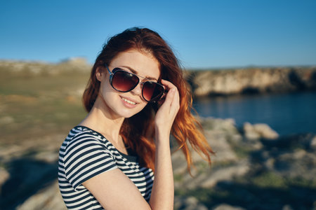 beautiful red-haired woman in a t-shirt and sunglasses on nature in the mountains near the riverの写真素材