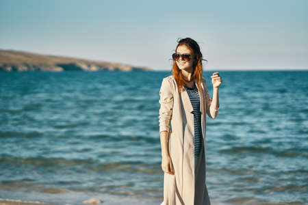 woman in coat and striped t-shirt on the beach sea waves landscape mountainsの写真素材
