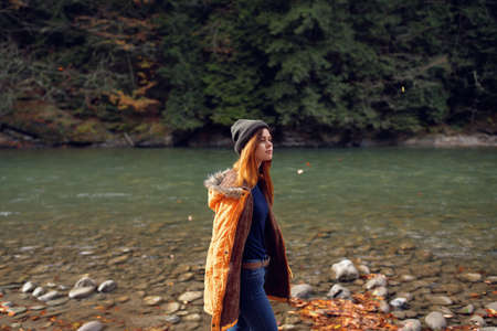 woman in a yellow jacket near the river admires nature Autumn forest