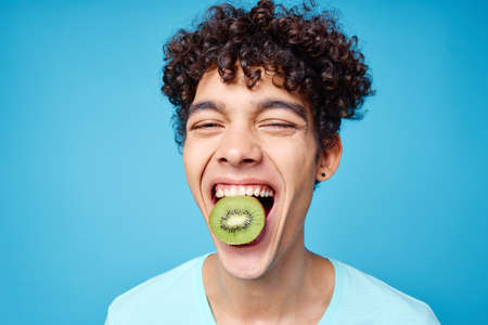 handsome man with kiwi curly hair in his mouth cropped view in blue backgroundの写真素材