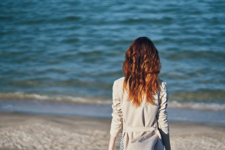 red-haired traveler in a coat and a t-shirt on the beach near the sea summer vacationの写真素材