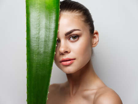 woman holding aloe leaf in front of her face and closed eyes clean skin cosmetologyの写真素材