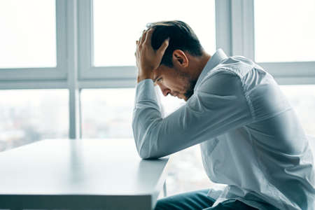 puzzled man sitting at a table room and holding his head with his hands