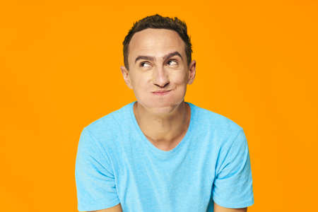 Cheerful man puffed out his cheeks and looks up on a yellow backgroundの写真素材