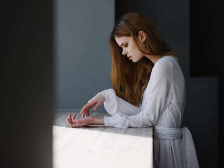 red-haired Woman in a white dress enriched herself on the windowsill near the window