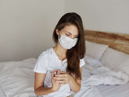 woman sitting in bed with thermometer under her arm checking temperatureの写真素材