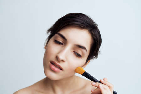 pretty brunette applying makeup on face close-up naked shouldersの写真素材