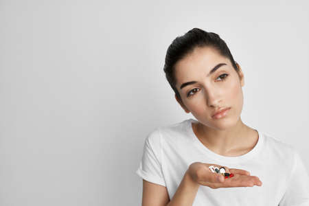woman in white t-shirt with pills in hands health problems medicineの写真素材