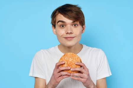 Man eating hamburger in white t-shirt diet food lifestyle blue background