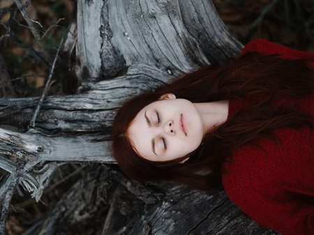 woman in red sweater with closed eyes Lies on the ground near a tree in the forestの写真素材