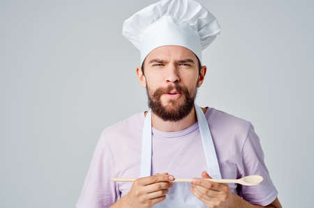 male chef in a white apron with a cap on his head with a spoon in his hands preparing foodの写真素材