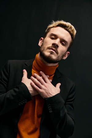 a man in an orange sweater and jacket on a dark background gestures with his handsの写真素材