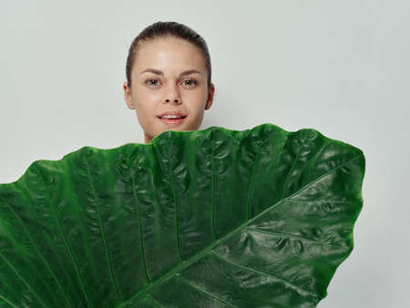 pretty woman covers her body with green leaf smile light backgroundの写真素材
