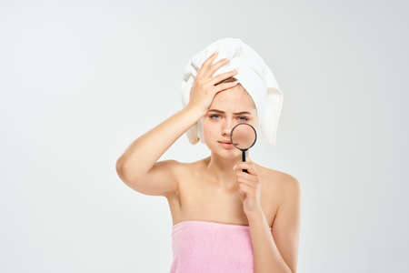 woman with bare shoulders holding a magnifying glass near face dermatology clear skinの写真素材