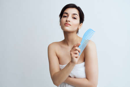 pretty woman with bare shoulders combing hair light background