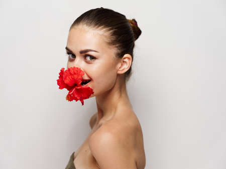 beautiful woman with red flower in her mouth naked shoulders studio light backgroundの写真素材