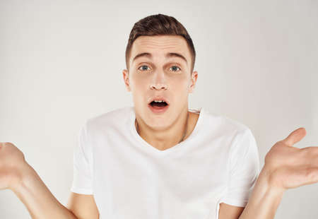 surprised man in white t-shirt throws up his hands emotions light backgroundの写真素材