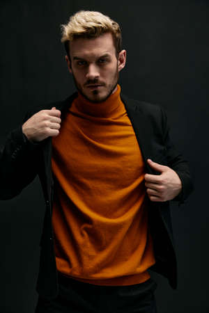 a man in an orange sweater and a jacket on a dark background blond portrait close-upの写真素材