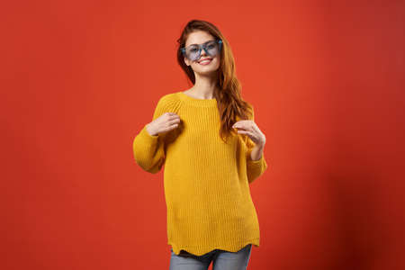 woman in a yellow sweater blue glasses studio fashionable hairstyle red backgroundの写真素材